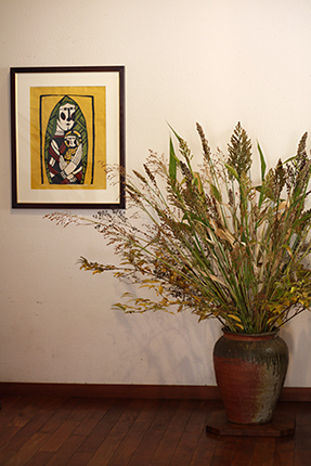 キビなど雑穀を中心に活けていただきました。壁面の作品は『聖母子』（渡辺禎雄 型染版画 1991）です